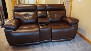 Ein braunes, hochverstellbares Sofa aus Leder mit Armlehnen und Getränkehaltern, platziert in einem Raum mit Holztüren und Fliesenboden.