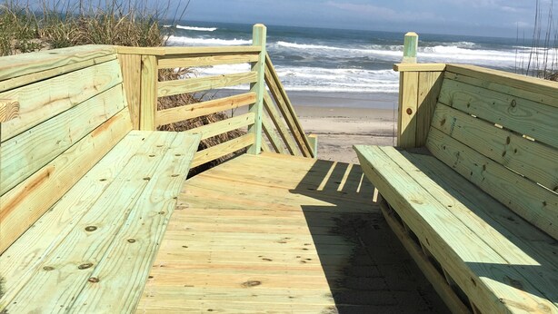 Une promenade en bois menant à la plage, avec des bancs de chaque côté.