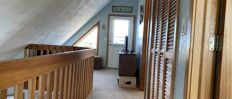 A narrow hallway with a wooden railing, a door with a 'Welcome Beach' sign, and a small desk with a computer.