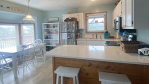 Une cuisine avec un îlot central en bois, des tabourets de bar blancs, un réfrigérateur et un coin repas avec une table et des chaises.