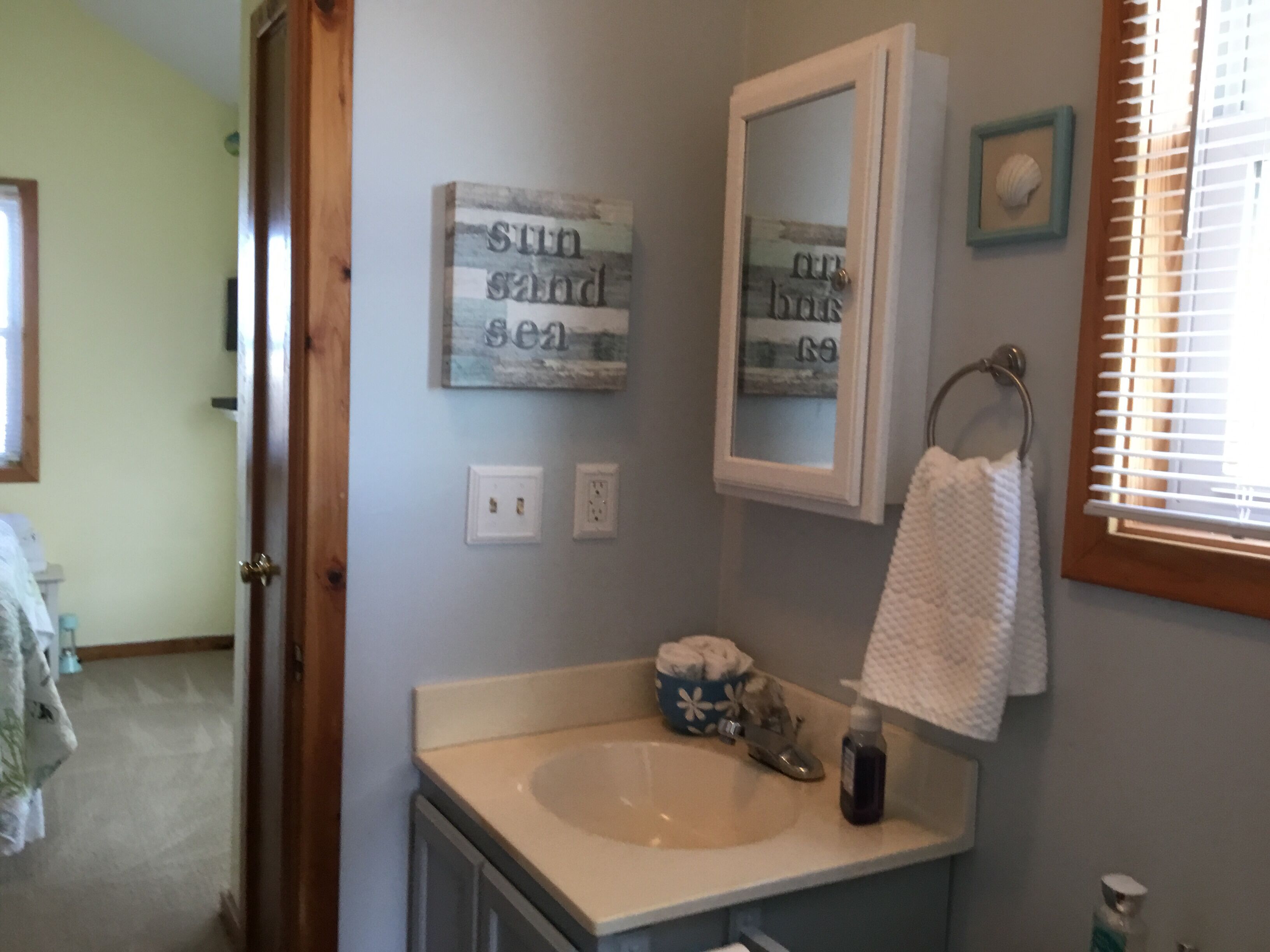 A bathroom with a sink, a mirror, and a towel rack. There are two wall-mounted light switches and a framed picture above the mirror.