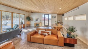 A spacious living room with a large leather sofa, a wooden ceiling, and a view of the outdoors through large windows. - Private Pool Paradise - MCM Luxury Black Hills (Nemo)
