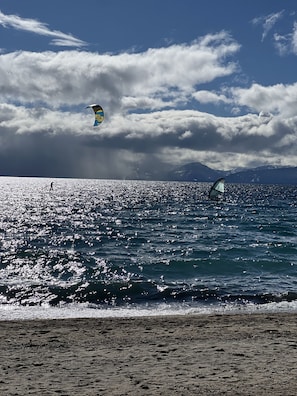 En strand med klar himmel och en person som utövar kitesurfing.
