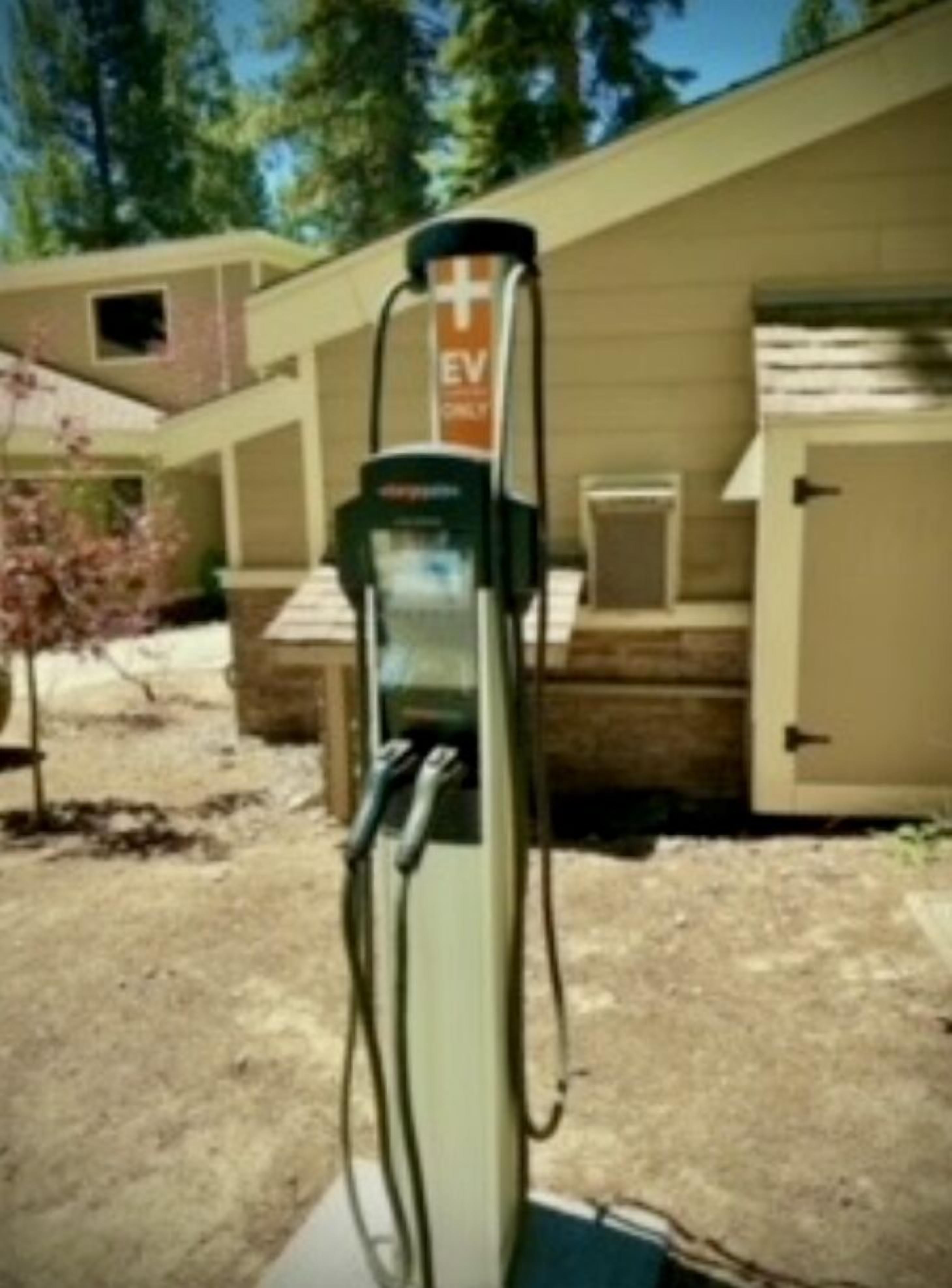 Una estación de carga para vehículos eléctricos en un área de estacionamiento con un edificio al fondo.