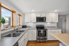 A modern kitchen with white cabinetry, stainless steel appliances, a double sink, and a window with a view of the outside.