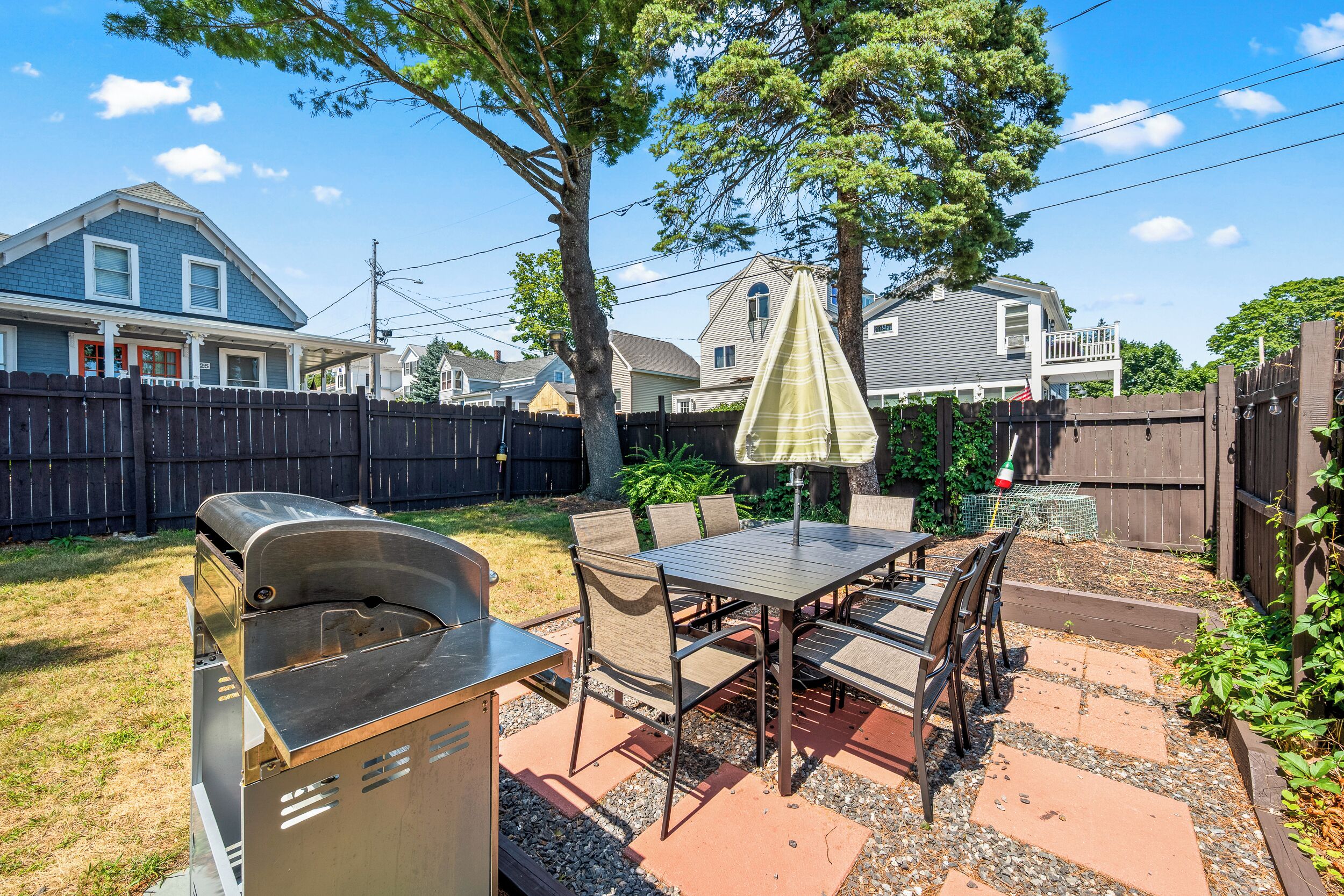 An outdoor patio with a grill, table, chairs, and a covered umbrella.