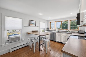 Eine moderne Küche mit einer zentralen Kochinsel, Barhocker, einem Geschirrspüler und Blick ins Freie durch große Fenster.
