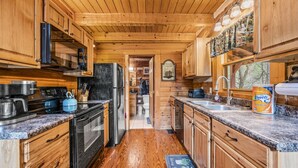 Interior de una cabaña de madera con cocina, que incluye estufa, refrigerador y alacenas de madera.