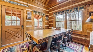 Interior de una cabaña de madera con una gran mesa de comedor, sillas y una alfombra.