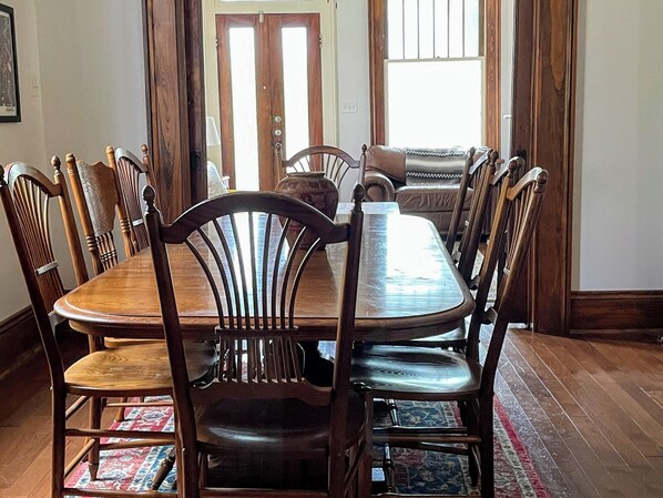 Een eetruimte met een houten tafel en stoelen, een vloerkleed en een bank op de achtergrond.