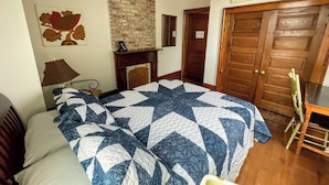 A bedroom with a bed, a nightstand, a lamp, a fireplace, a wooden door, and a ceiling fan.