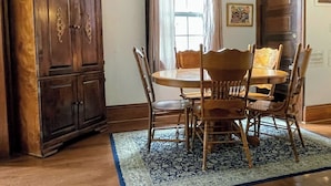A dining area with a round table, six wooden chairs, a dark wooden cabinet, and a patterned rug.
