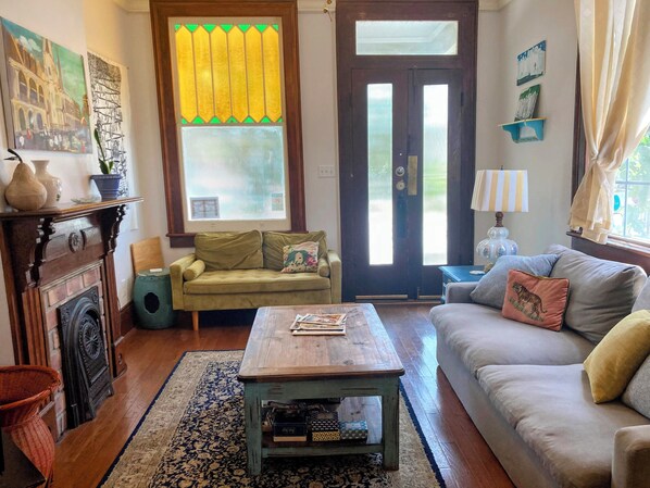 A cozy living room with a fireplace, a sofa, a coffee table, and a window with curtains.