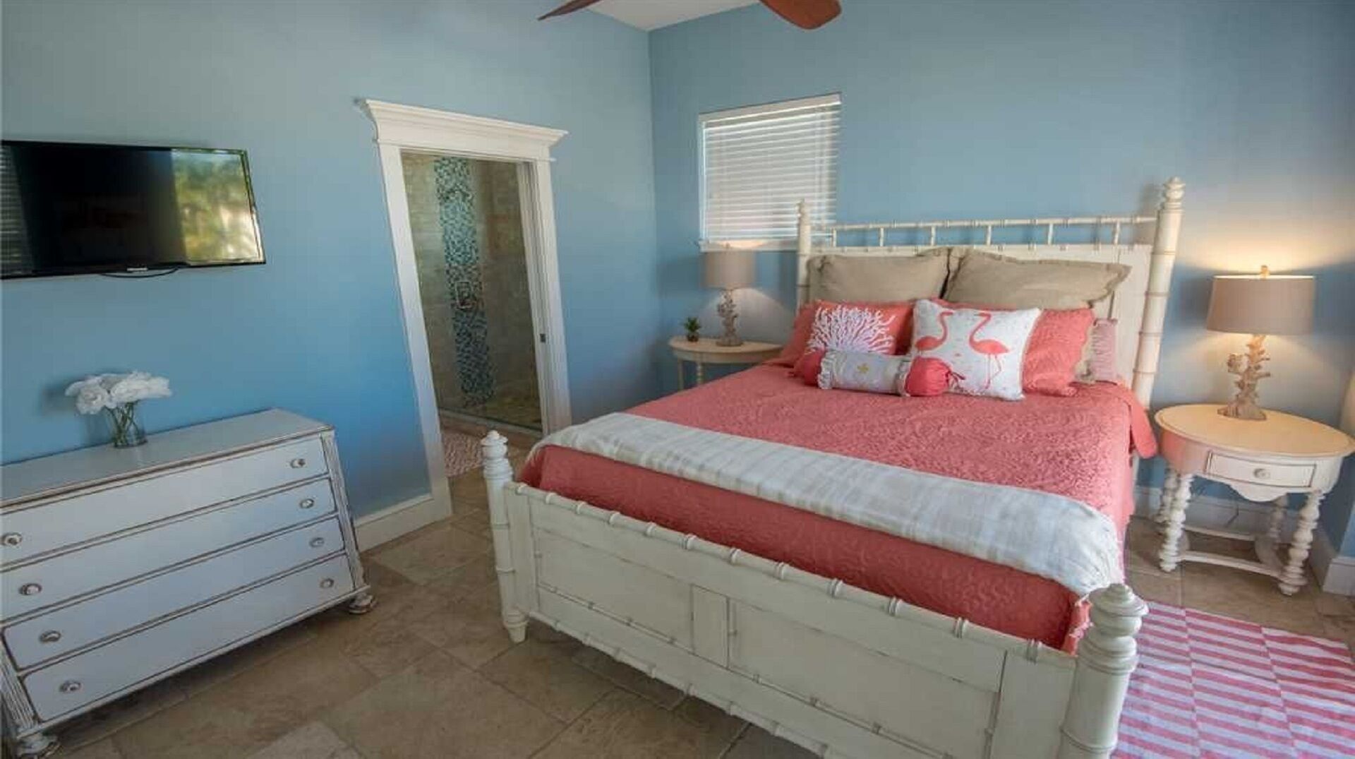 Une chambre à coucher avec un lit, une commode, une télévision et une fenêtre avec des stores.