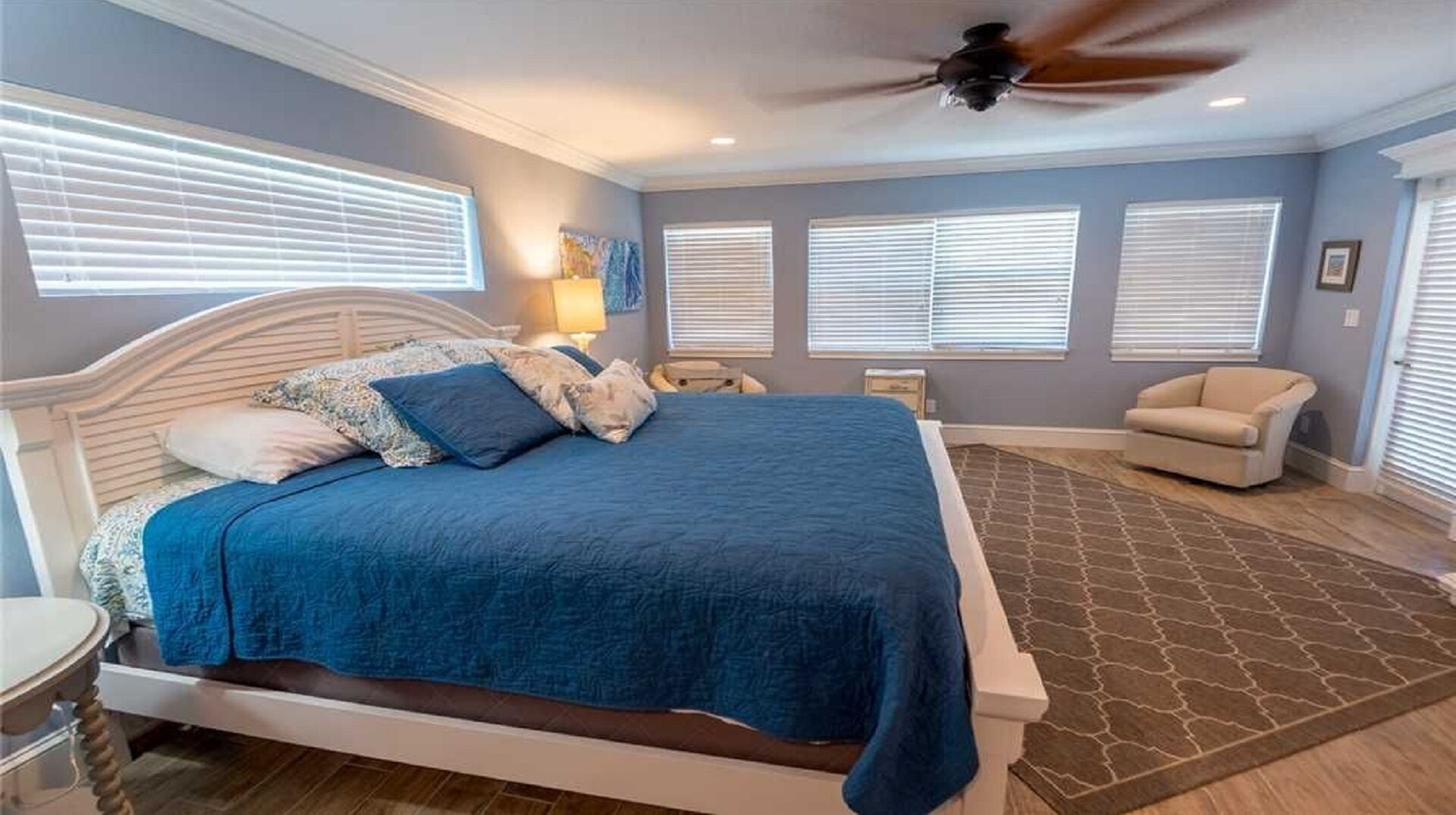 A bedroom with a large bed, a ceiling fan, and multiple windows with blinds.