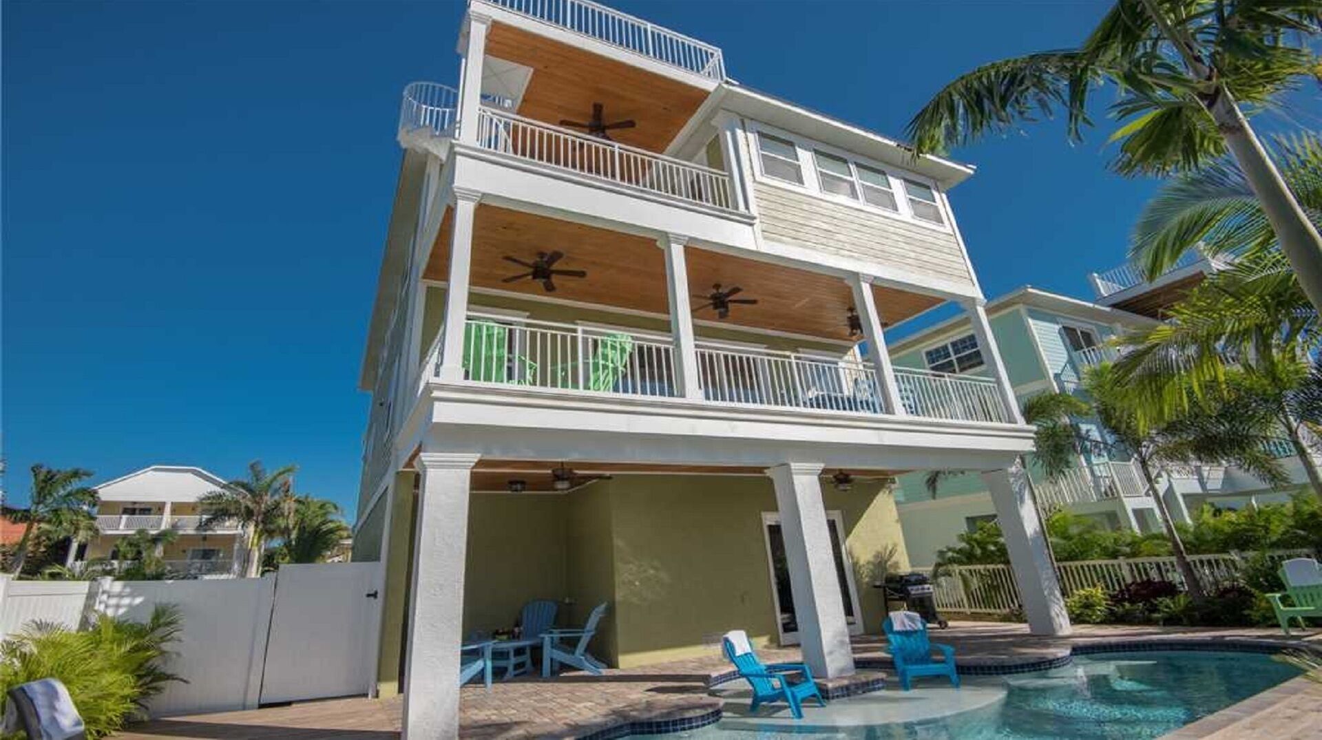 Una casa de dos pisos con piscina, balcones y mobiliario exterior.