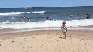 A sandy beach with people swimming and surfing, and a boat in the distance. - Highly rated, clean, ground floor condo w/pool; steps to beach. (Virginia Beach)