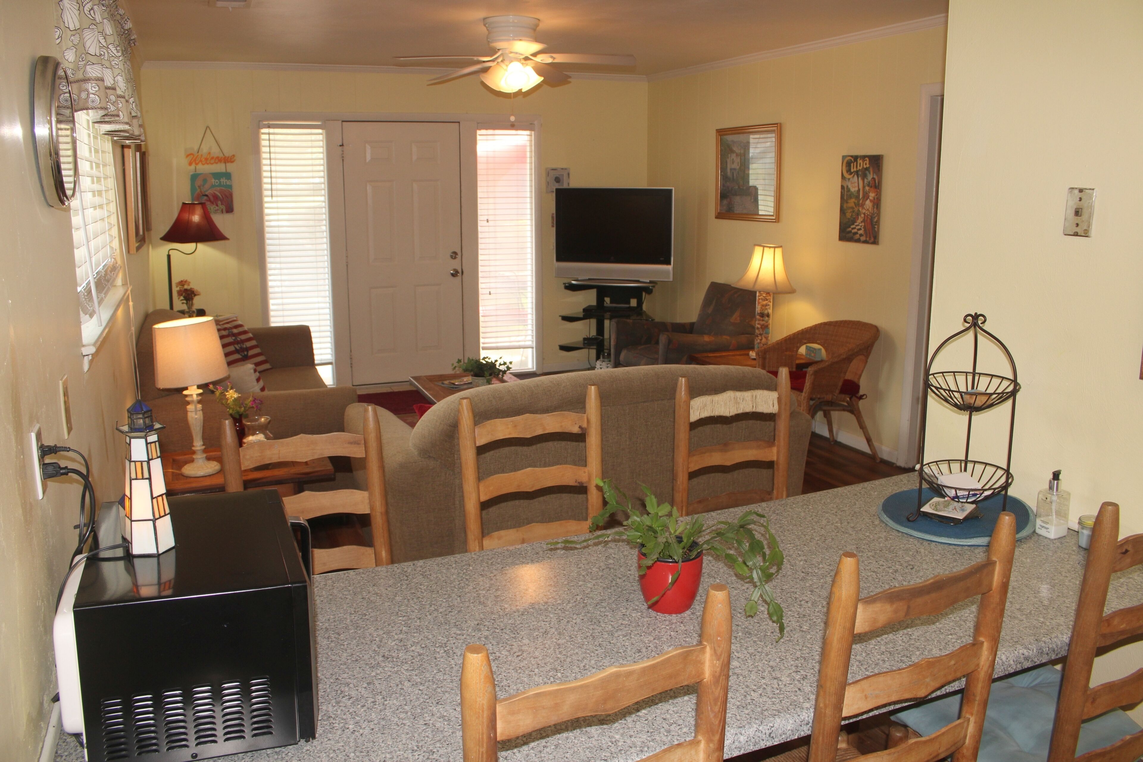 A living room with a television, a ceiling fan, and a dining area with wooden chairs and a granite table.