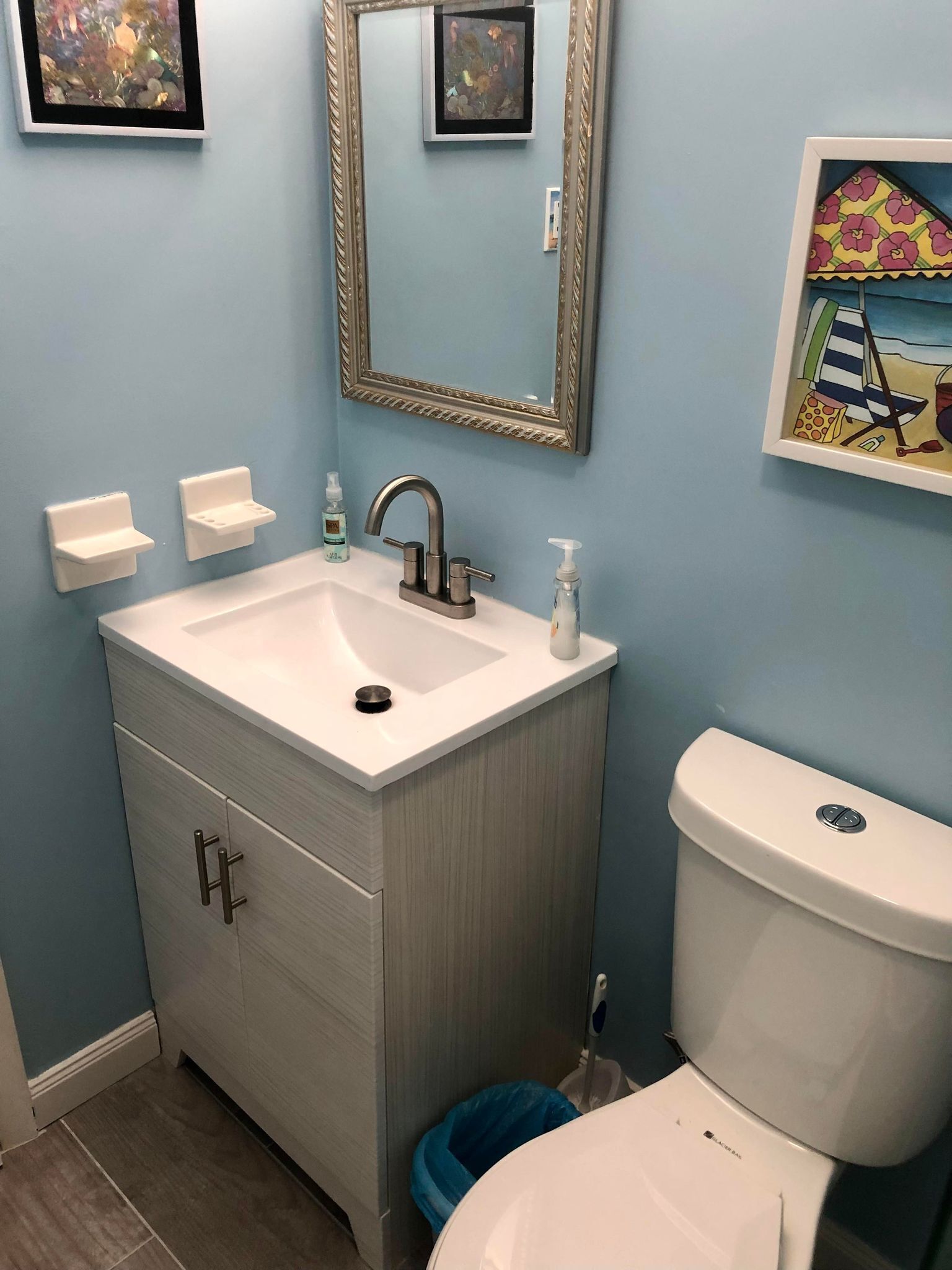 A bathroom with a white sink, a mirror, a toilet, and a blue trash bin.