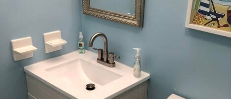 A bathroom with a white sink, a mirror, a toilet, and a blue trash bin.