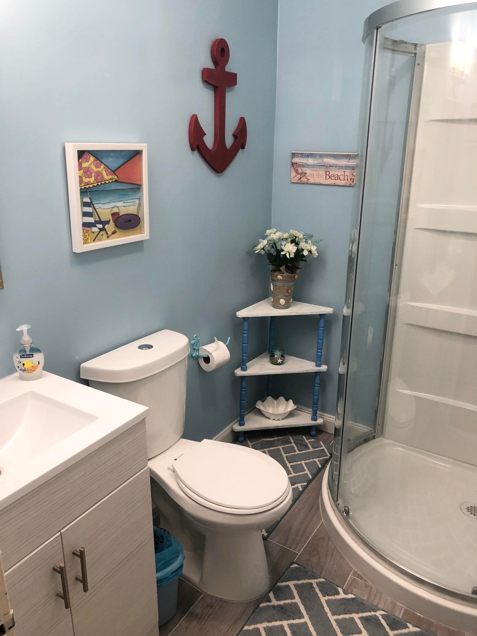 A bathroom with a toilet, sink, shower, and decorative items including a beach-themed painting and an anchor.