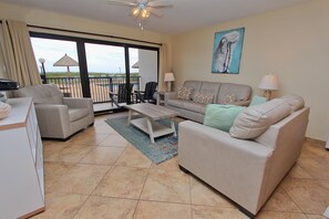 A spacious living area with a sofa, chairs, a coffee table, and a view of the outdoors through a sliding glass door. - Ocean's Edge - Condo 103: Spacious 2BR ground floor condo (South Padre Island)