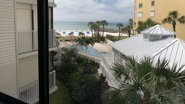 A view of a beach resort with a pool, palm trees, and a clear sky.