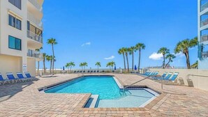 A pool area with blue chairs, palm trees, and a clear sky.