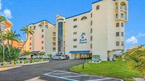 A multi-story hotel with a prominent 'Beach Palms' sign, a parking lot, and a well-maintained lawn with palm trees.