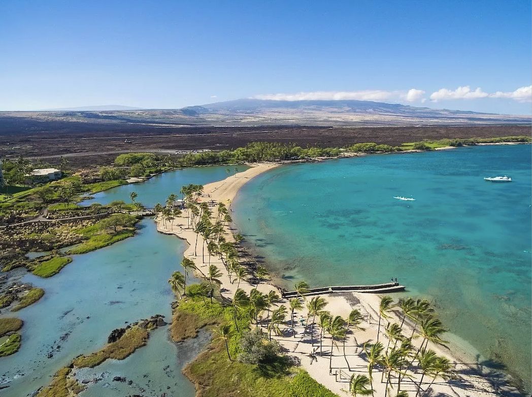 Vue aérienne d’une zone côtière avec des eaux turquoise limpides, une plage de sable et un petit bateau.
