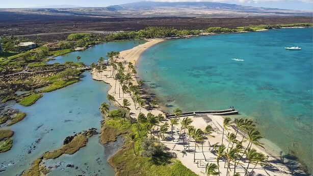 Vue aérienne d’une zone côtière avec des eaux turquoise limpides, une plage de sable et un petit bateau.