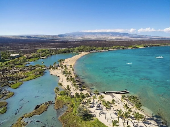 An aerial view of a coastal area with clear turquoise waters, a sandy beach, and a small boat.