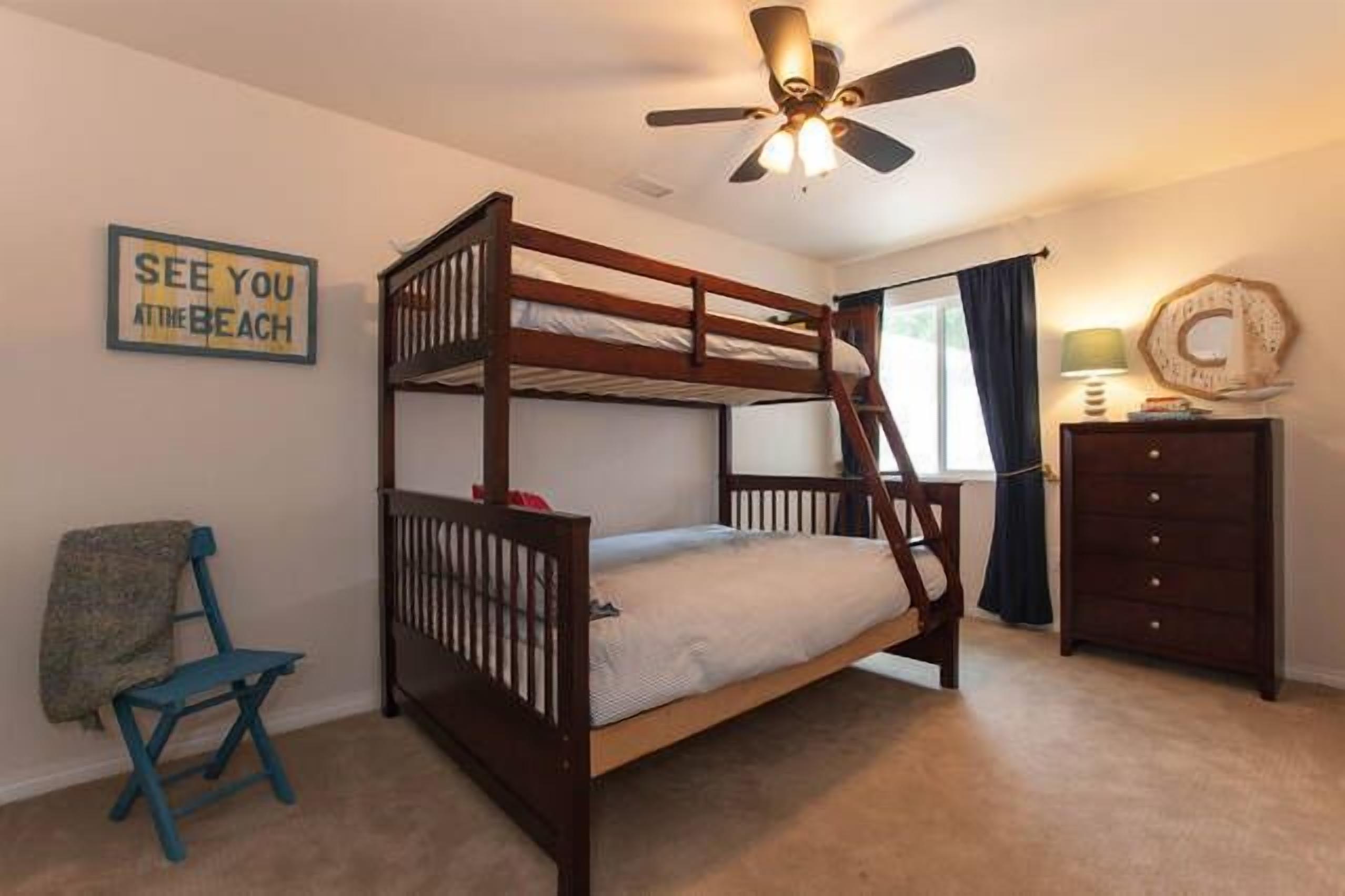 A bunk bed room with a ceiling fan, a chair, a dresser, and a wall sign.