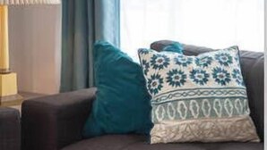 A living room with a dark sofa, a patterned pillow, a wooden tray, and a lamp. - Family Friendly Beach House - Rare Central Air Conditioning, Close to Town/Beach (Carlsbad)