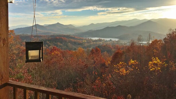Un balcon en bois orné d’une lanterne suspendue, d’où l’on peut admirer un paysage montagneux aux couleurs automnales et un lac.