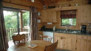 Une cabane en bois comprenant un coin repas, une cuisine et offrant une vue sur la forêt.