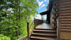 Un escalier en bois mène à un chalet en rondins doté d’un porche, le tout étant entouré d’une végétation luxuriante.