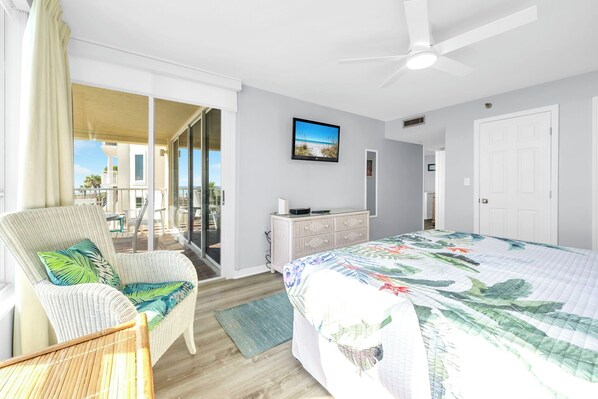 A bedroom with a bed, a chair, a dresser, a television, and a sliding glass door leading to a balcony.