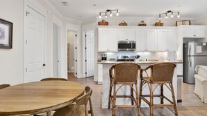 A modern kitchen with white cabinets, a central island with chairs, and a dining table.