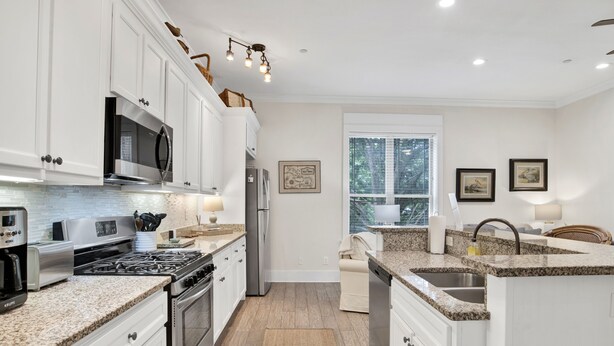 A modern kitchen with white cabinetry, granite countertops, stainless steel appliances, and a large window providing natural light.