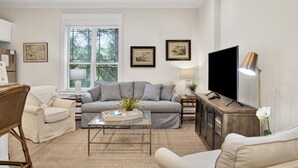 A living room with a sofa, armchairs, a coffee table, a TV, and framed pictures on the wall.