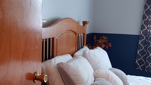 Une chambre à coucher avec une tête de lit en bois, un lit agrémenté de plusieurs oreillers, une moquette foncée et un mur d’accent bleu.
