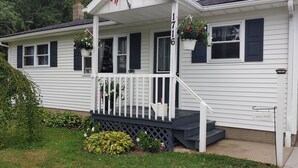 Une maison blanche avec des volets noirs, une véranda dotée d’une balustrade blanche et une pancarte sur laquelle on peut lire « BIENVENUE ».