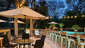 An outdoor patio with wooden flooring, round tables, chairs, and umbrellas. - Wondercove, 7 Rustic Cozy Cottages, Secluded & Sleeps up to 54, on Lake Dunlap (New Braunfels)