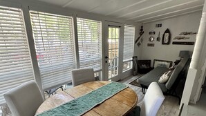 A dining area with a wooden table, white chairs, and a green runner. There is a sofa and a small table with a lamp in the background. - Wondercove, 7 Rustic Cozy Cottages, Secluded & Sleeps up to 54, on Lake Dunlap (New Braunfels)