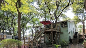 A rustic cabin with a wooden staircase and a red umbrella, surrounded by lush greenery and trees. - Wondercove, 7 Rustic Cozy Cottages, Secluded & Sleeps up to 54, on Lake Dunlap (New Braunfels)