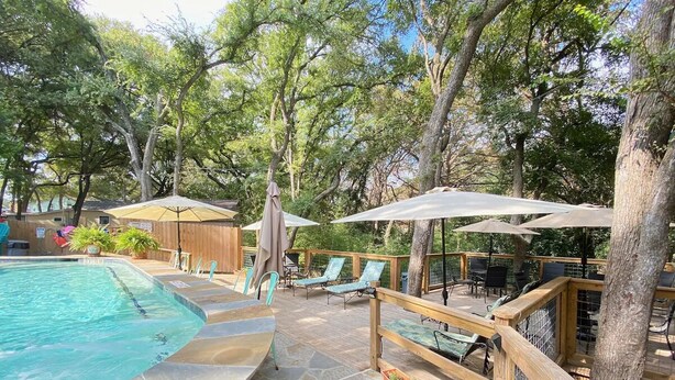 A pool area with a stone deck, lounge chairs, and umbrellas. - Wondercove, 7 Rustic Cozy Cottages, Secluded & Sleeps up to 54, on Lake Dunlap (New Braunfels)