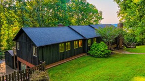 A two-story wooden house with a dark roof, surrounded by a well-maintained lawn and dense trees. - 5 BR, 3 King Beds, Fire Pit, Hot Tub, Game room! Amazing Year Round Lake View!! (Sparta)