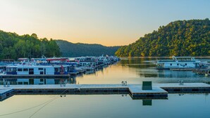 A marina with multiple boats docked, calm water, and a forested hillside in the background. - 5 BR, 3 King Beds, Fire Pit, Hot Tub, Game room! Amazing Year Round Lake View!! (Sparta)