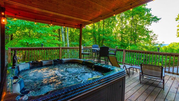 A hot tub on a wooden deck with a view of trees. - 5 BR, 3 King Beds, Fire Pit, Hot Tub, Game room! Amazing Year Round Lake View!! (Sparta)
